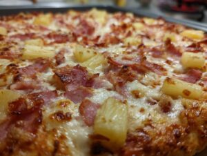 Close-up of a freshly baked Hawaiian pizza with melted cheese, ham, and pineapple chunks.