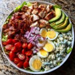 A vibrant and hearty Cobb salad featuring chopped chicken, crispy bacon, hard-boiled eggs, cherry tomatoes, red onion, avocado, and blue cheese.