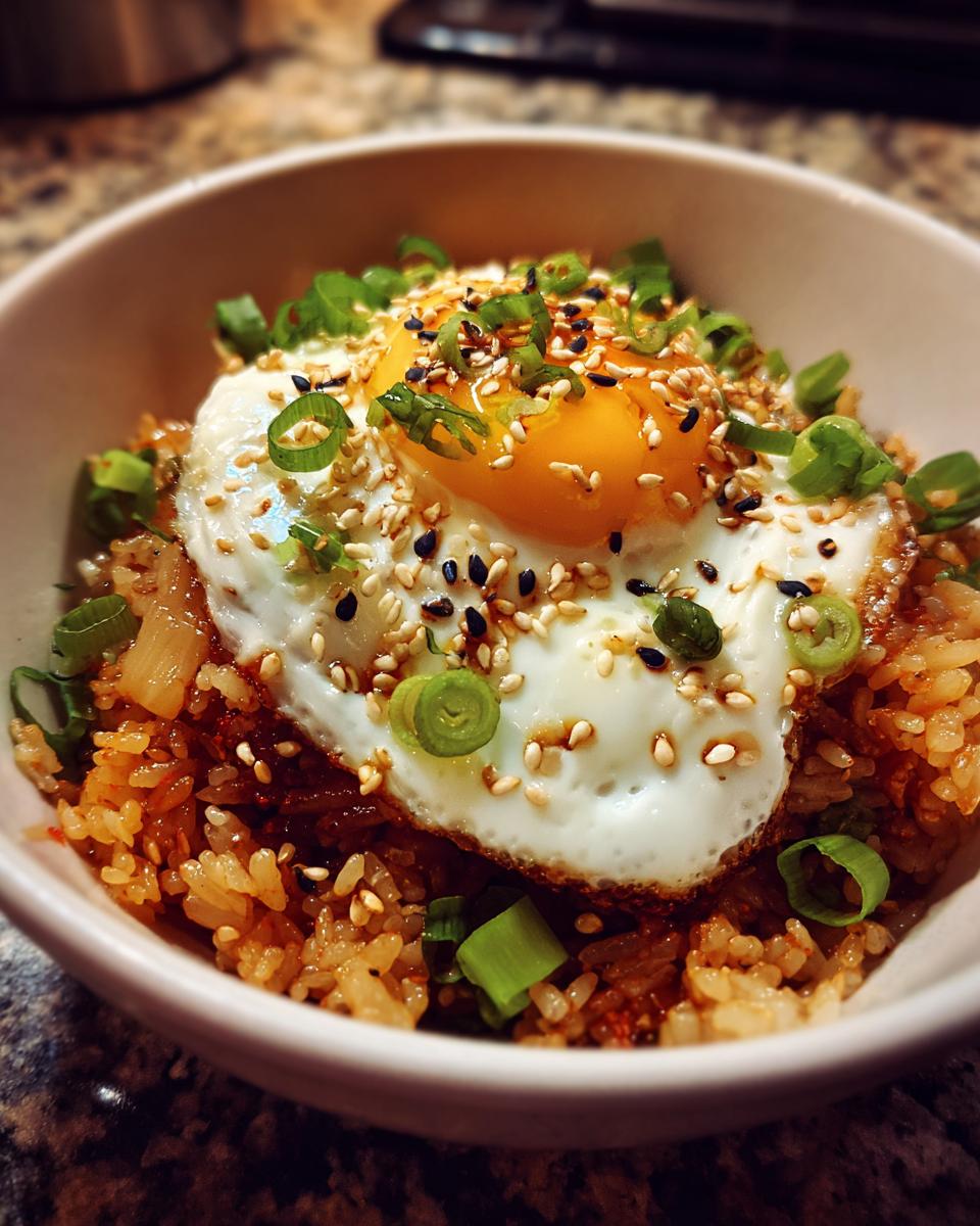A bowl of spicy Kimchi fried rice topped with a perfectly fried egg, green onions, and sesame seeds.