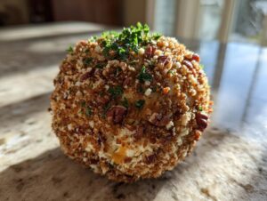 Close-up of a round cheese ball coated in crunchy nuts, breadcrumbs, and fresh parsley.