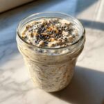 Close-up of creamy overnight oats in a glass jar, topped with chia seeds and granola.