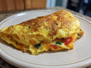 A golden-brown, folded omelette filled with melted cheese, diced tomatoes, and spinach, served on a plate.