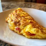 A golden brown omelette filled with melted cheese and diced tomatoes, served on a white plate.