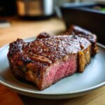A juicy, perfectly cooked ribeye steak slice with a beautiful pink center and a seared crust, served on a plate.