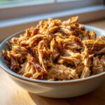 A close-up shot of a bowl filled with tender and crispy pork carnitas, ready to be served.
