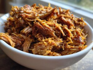 Close-up of a white bowl filled with shredded, tender, and crispy pork carnitas.