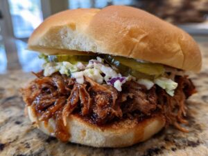 A close-up of a mouthwatering pulled pork sandwich piled high with tender shredded pork, creamy coleslaw, and pickles on a soft bun.