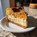 A perfect slice of pumpkin cheesecake with a creamy white layer and a rich pumpkin layer, topped with cinnamon.