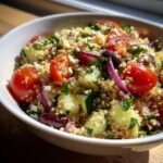 A vibrant bowl of quinoa salad featuring cherry tomatoes, cucumber, red onion, olives, and feta cheese.