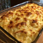 Close-up of bubbly, golden-brown baked scalloped potatoes in a glass dish, sprinkled with herbs.