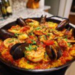 A close-up of a flavorful seafood paella in a pan, featuring shrimp, mussels, and rice.