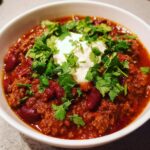 A bowl of hearty slow cooker chili topped with sour cream and fresh cilantro.