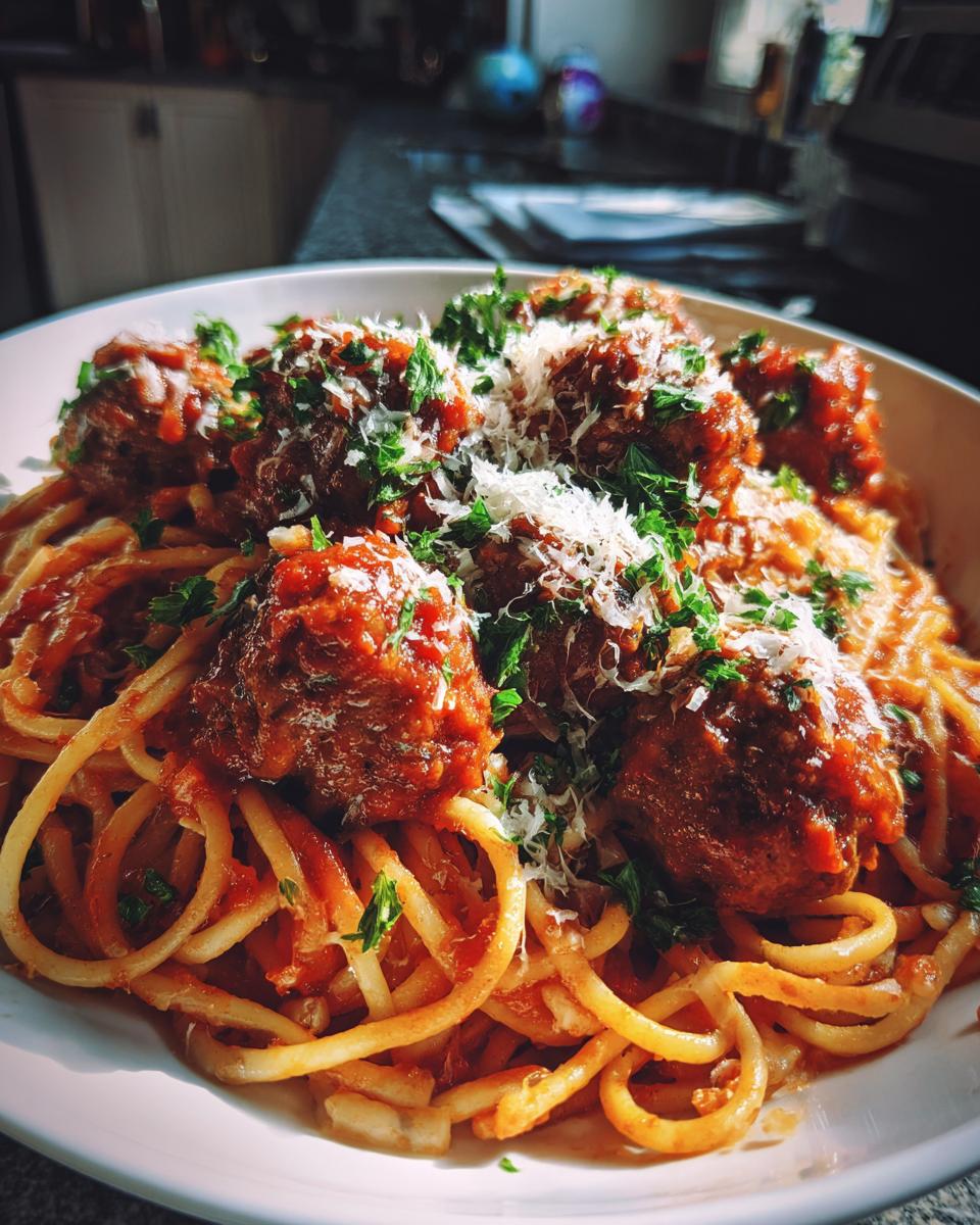 A close-up of a bowl of spaghetti and meatballs, topped with grated Parmesan cheese and fresh parsley.