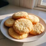A pile of golden brown sugar cookies with a slightly cracked surface, presented on a white plate.