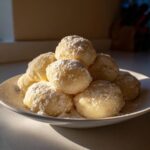 A pile of tender potato gnocchi dusted with powdered sugar on a white plate.