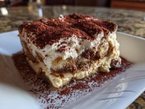 A close-up of a decadent slice of Tiramisu, layered with ladyfingers and cream, dusted with cocoa powder.
