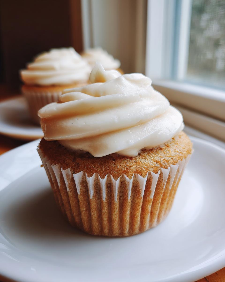 Close-up of a perfect vanilla cupcake topped with swirls of creamy white frosting.