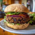 A close-up of a homemade veggie burger on a bun, layered with lettuce, tomato, red onion, and a hearty patty.
