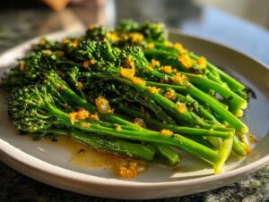 Close-up of vibrant green broccolini stalks glistening with a light sauce and topped with orange zest.