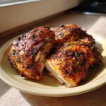 Three pieces of perfectly roasted greek chicken with deeply browned, herbed skin served on a light yellow plate.