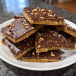A stack of homemade graham cracker toffee squares topped with melted chocolate and chopped nuts on a white plate.