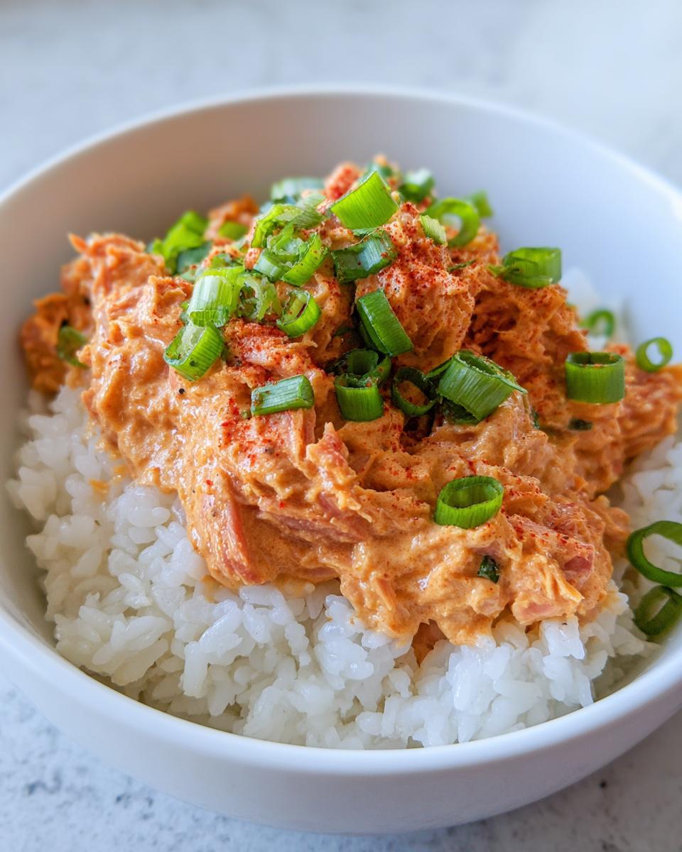 A close-up of creamy, orange-tinted tuna rice topped with fresh green onions and paprika.