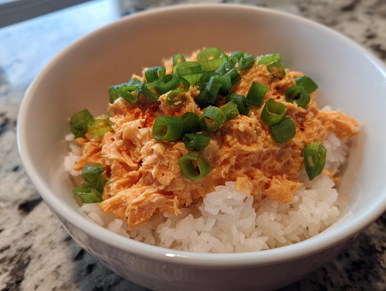 Close-up of a white bowl filled with white rice and topped generously with spicy tuna rice mixture and sliced green onions.