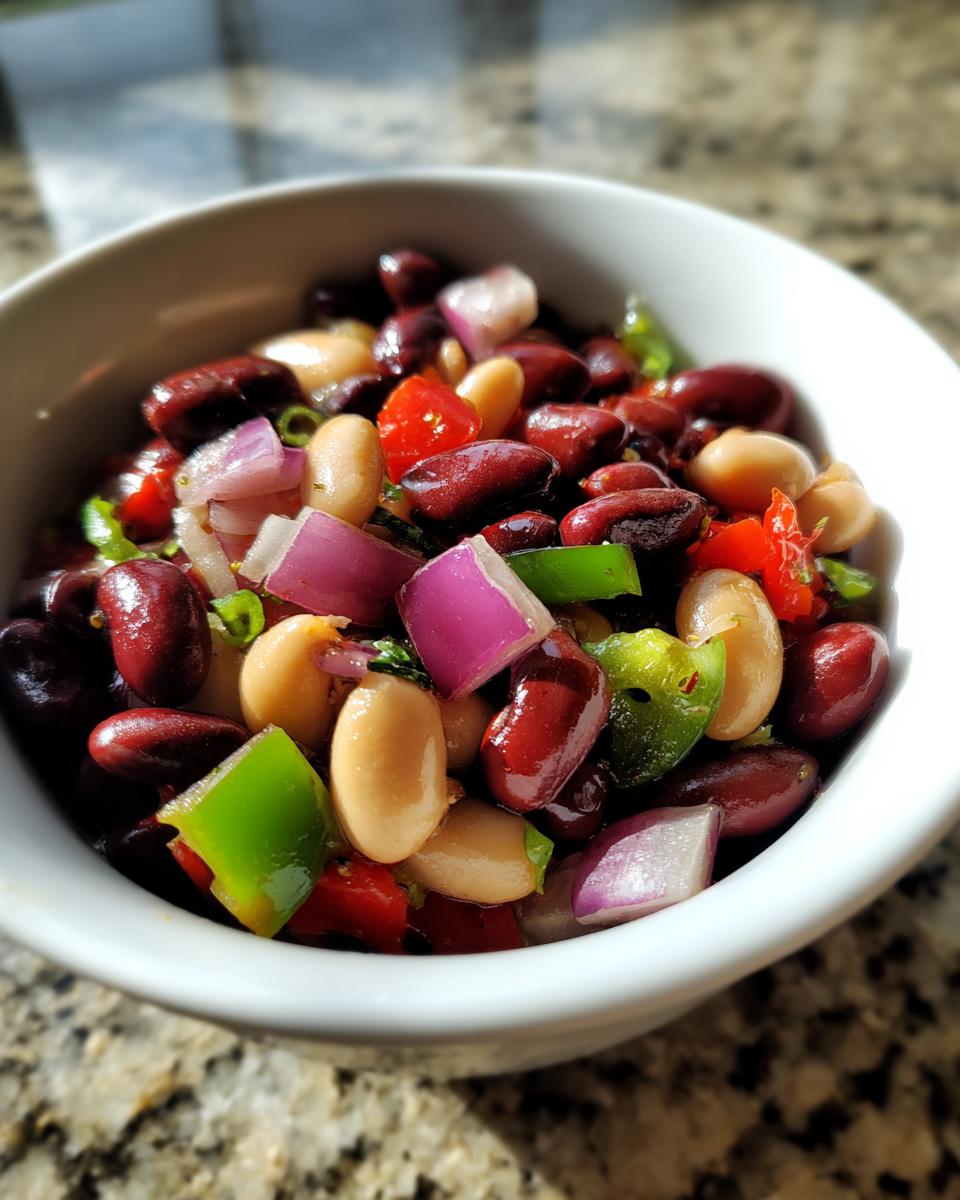 Close-up of a white bowl filled with colorful bean salad featuring kidney beans, white beans, red onion, and green peppers.