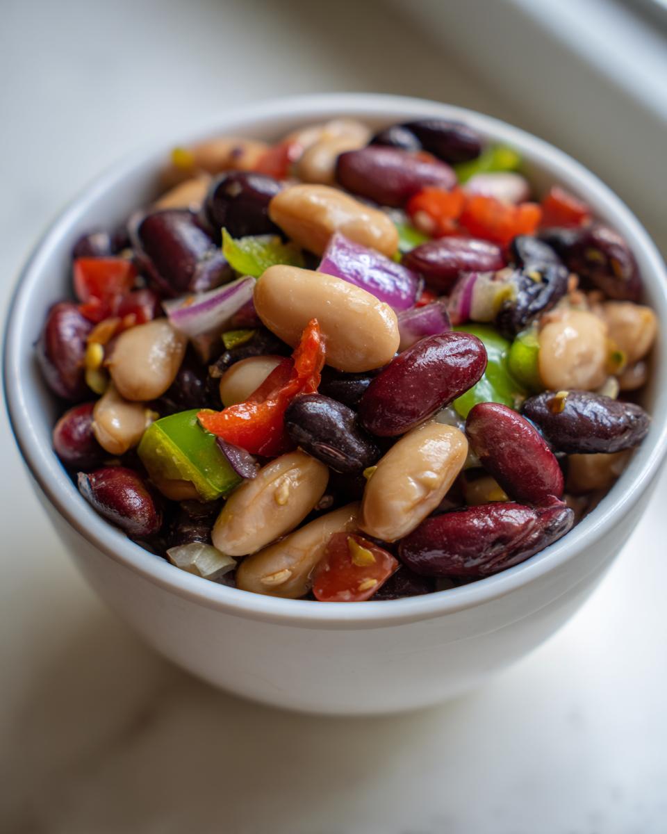 Close-up of a vibrant mixed bean salad featuring kidney, black, and white beans with chopped red onion and peppers.