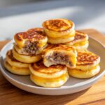 A stack of golden brown McGriddle bites filled with sausage and melted cheese, one is bitten into.
