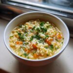 A close-up of a bowl of amazing pastina soup, featuring small pasta, diced carrots, topped with Parmesan cheese and fresh parsley.