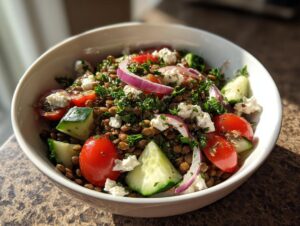 A close-up of a vibrant lentil salad featuring brown lentils, cherry tomatoes, cucumber chunks, red onion, and feta cheese.