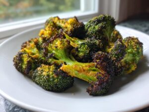 Close-up of perfectly seasoned and charred roasted broccoli on a white plate, ready to eat.