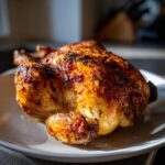A beautifully browned, whole roasted chicken with crispy skin resting on a white plate.