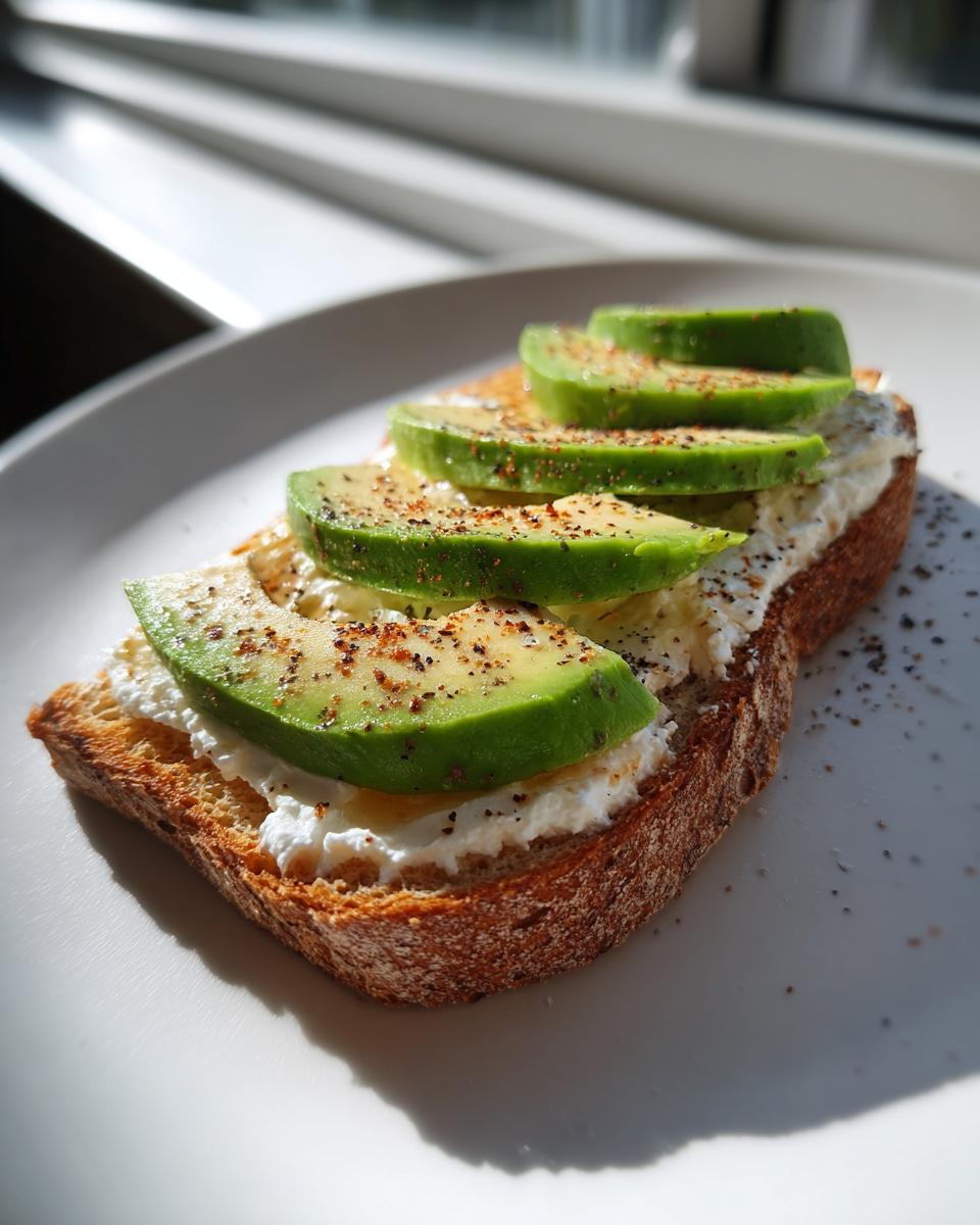 A slice of toasted bread topped with cottage cheese, sliced avocado, and sprinkled with pepper for a delicious cottage cheese toast.