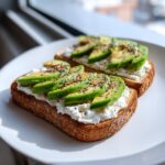 Two slices of cottage cheese toast topped with fresh avocado slices and cracked black pepper.
