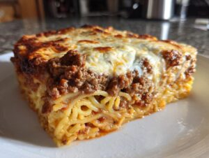 Close-up of a thick slice of baked spaghetti pie featuring layers of pasta, rich meat sauce, and melted, browned cheese topping.