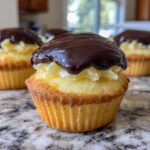 A close-up of one of the delicious Boston Cream Pie Cupcakes topped with vanilla cream filling and rich chocolate ganache.