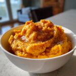 A white bowl filled with vibrant orange mashed sweet potatoes, topped with melted butter and cinnamon.