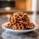 A tempting pile of homemade butter toffee pretzels coated in a shiny, rich caramel glaze, served on a white plate.