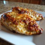 Two golden-brown, seasoned caesar chicken breasts resting on a white plate.