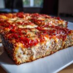 A thick slice of chicken crust pizza showing the meat base, melted cheese, and rich tomato sauce topping.