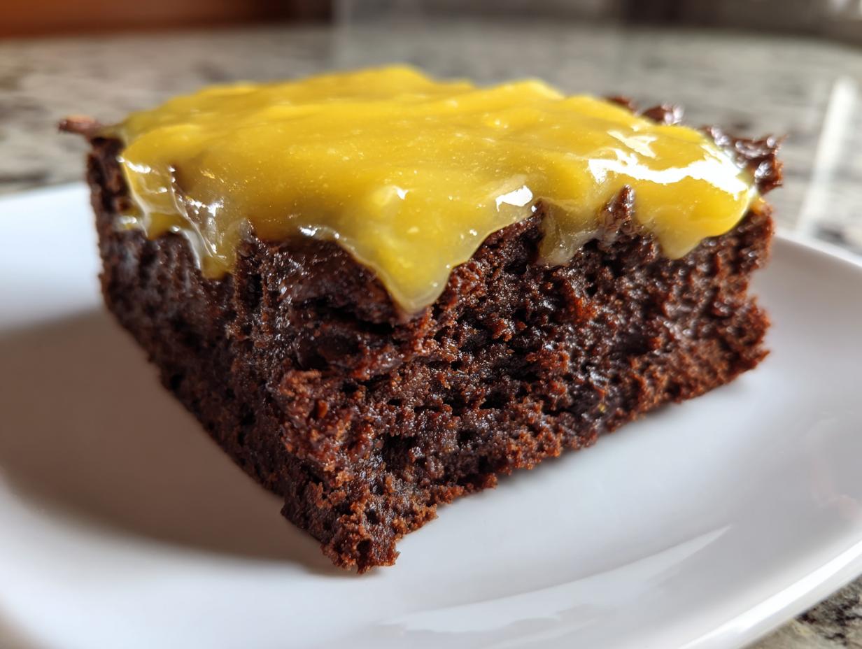 Close-up of a rich, dark chocolate brownie square topped with a thick layer of bright yellow lemon frosting, perfect for lemon brownies.