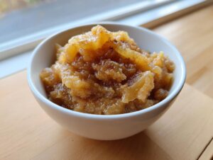 Close-up of chunky, spiced homemade applesauce served in a small white bowl on a wooden surface.
