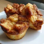 Three golden brown french toast muffins topped with cinnamon sugar, served on a white plate.