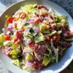 A vibrant, close-up view of a hearty grinder salad tossed in creamy dressing, featuring salami, olives, and red onion.