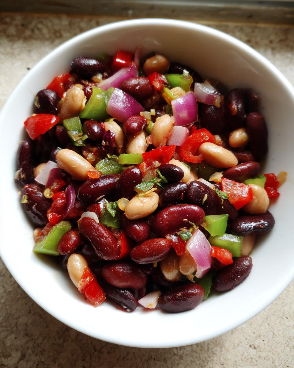 Overhead view of a vibrant three bean salad featuring kidney beans, white beans, red onion, and bell peppers in a white bowl.