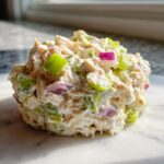 A close-up mound of creamy cottage cheese chicken salad mixed with bright green celery and purple red onion.