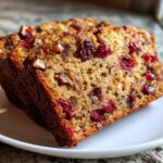 Close-up of two thick slices of moist cranberry walnut bread showing visible dried cranberries and chopped walnuts.