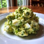 A close-up of a generous scoop of creamy avocado egg salad with visible chunks of hard-boiled egg and green onions.